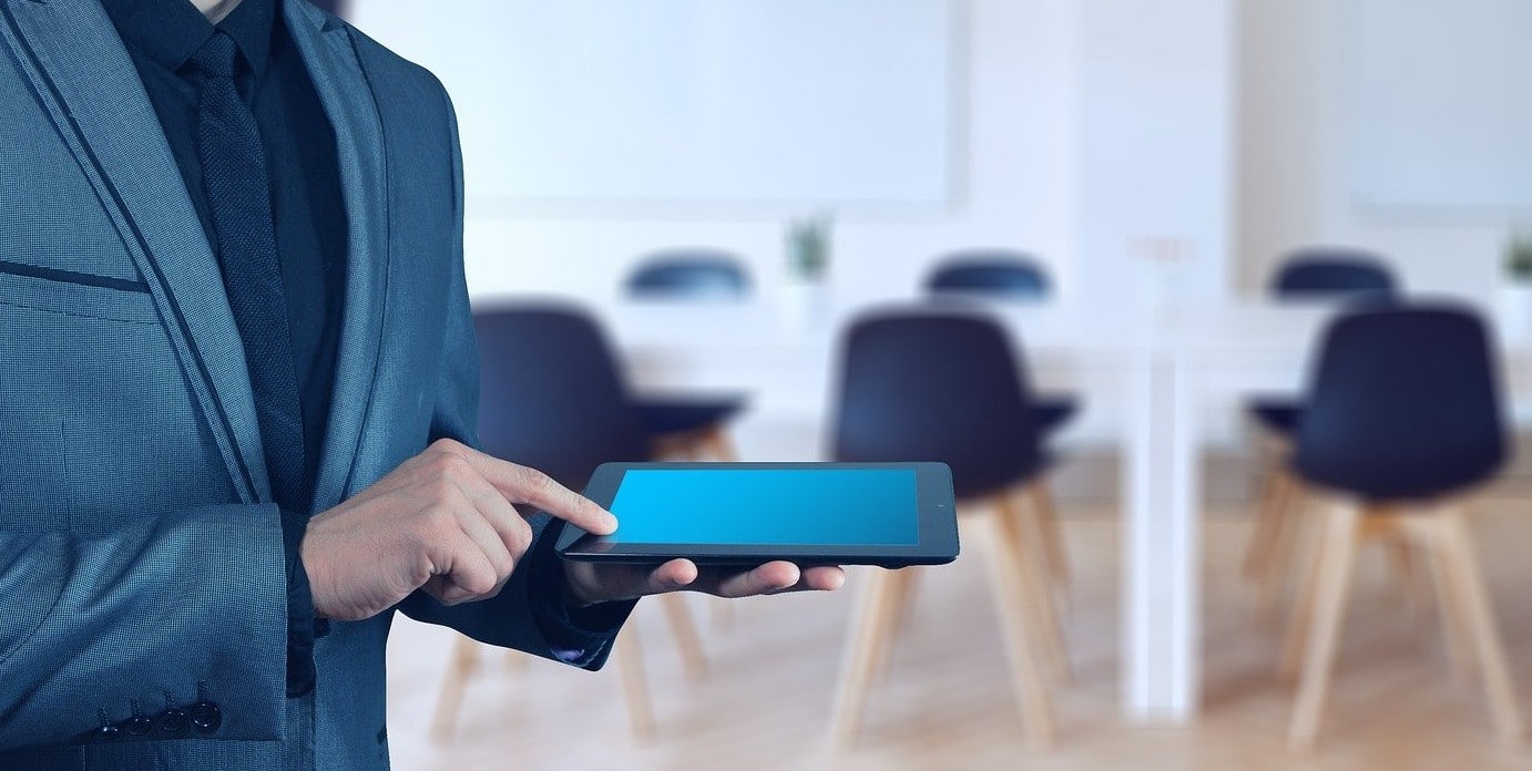 Homem de terno com tablet na mão e sala de reunião de fundo